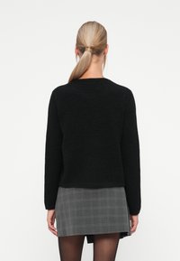 Black, textured sweater with long sleeves, crew neckline. Paired with a gray plaid skirt, showcasing a simple and modern design.
