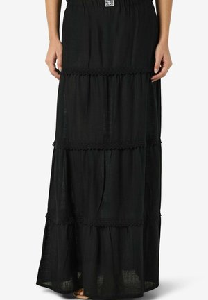 Svart lagdelt maxiskjørt med blonder, elastisk midjebånd, båret av en person som står med armene avslappet ned langs siden.