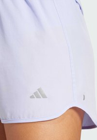 Pantalones cortos deportivos de un suave color lavanda, hechos de tela lisa, con un sutil logo plateado reflectante y un dobladillo curvado.