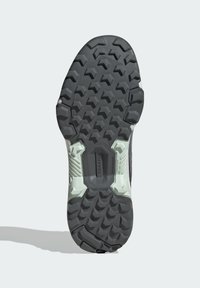 Talpa unei încălțări de alergare din cauciuc negru, cu un model hexagonal texturat, având accente de tracțiune albe pe laterale și un design robust.