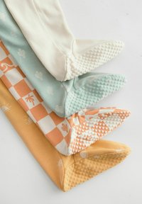 Quatre paires de collants doux et colorés : crème, vert menthe, à carreaux orange et jaune, chacun avec des semelles texturées et antidérapantes ainsi que des motifs amusants.