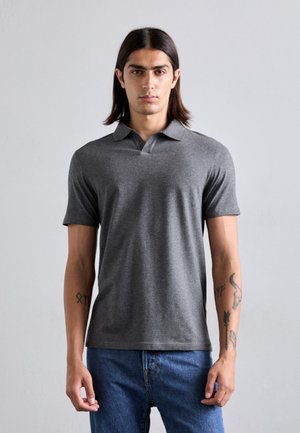 Grijze polo met een klassieke kraag en korte mouwen, gemaakt van zachte stof; gecombineerd met blauwe jeans en opvallende tatoeages op de armen.