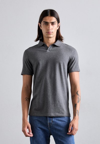 Polo grigio con colletto classico e maniche corte, realizzato in tessuto morbido; abbinato a jeans blu e con tatuaggi visibili sulle braccia.