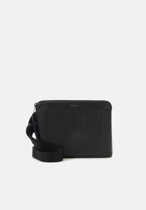 Sac bandoulière rectangulaire noir avec des rayures verticales, une large bandoulière en tissu et un petit logo centré près de la fermeture éclair supérieure.