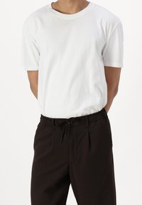 Biała bawełniana koszulka z krótkim rękawem i okrągłym dekoltem, zestawiona z czarnymi spodniami na troczki o luźnym kroju i bocznymi kieszeniami.