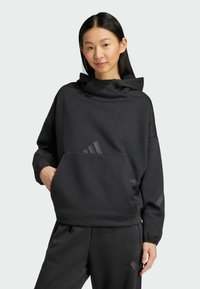 Crna dukserica s visokim ovratnikom i prednjim džepom. Ima suptilne logotipove i opušteni kroj. Izrađena je od mekog, glatkog materijala.