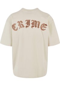 Beige oversized T-shirt med ordet "CRIME" i stor, stiliseret brun skrift på ryggen. Lavet af blødt bomuldsmateriale.