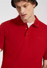 Czerwona bawełniana koszulka polo z złożonym kołnierzykiem, zapięciem na dwa guziki i krótkim rękawem. Posiada subtelne logo na klatce piersiowej.