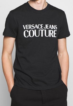 Black cotton t-shirt featuring bold white text "VERSACE JEANS COUTURE" across the chest, short sleeves, and a classic crew neckline.