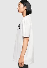Witte katoenen t-shirt met een losse pasvorm, voorzien van een ronde hals en korte mouwen. Zwart logo tekst aan de voorkant. Soepele textuur.