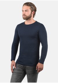 Navyblå langærmet t-shirt lavet af bomuld, med rund halsudskæring og tætsiddende silhuet, parret med mørke jeans.