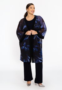 Gennemsigtig sort kimono med blå blomstermønstre, åben front og brede ærmer. Bærer den med en navy top og sorte bukser; sølv hæle.