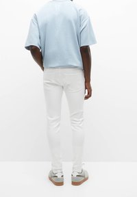 Lichtblauwe oversized t-shirt, witte slim-fit jeans en grijze sneakers met bruine zolen, gezien vanuit de rug. Glad materiaal en eenvoudig ontwerp.