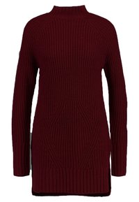 Långärmad burgunderröd tröja med hög krage, ribbat tyg och tydliga vertikala mönster. Har sidoflikar vid fållen.