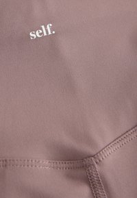 Sportkangas tolmuse malva värviga, sileda tekstuuriga. Kaunistatud valge tekstiga "self.". Sisaldab korrapäraseid õmbluse detaile.