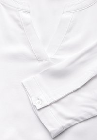 Weißes Shirt mit V-Ausschnitt, langen Ärmeln mit Knopfmanschetten, glatter Textur und subtilen Nahtdetails.