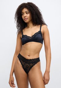 Lace-trimmed black bra and thong set. Bra features adjustable straps and structured cups; thong has sheer lace with decorative border.