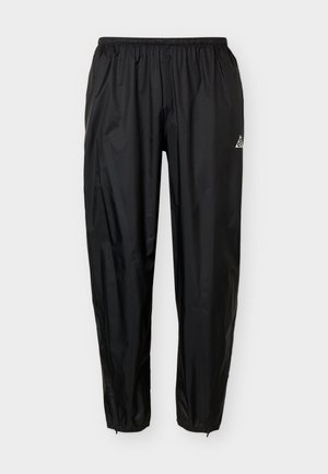 Zwarte lichte sportbroek met elastische tailleband en enkelsluitingen, met een klein wit logo op de rechterdij.