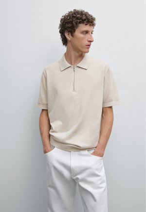 Beige kortærmet polo T-shirt med lynlåskrave, lavet af blødt materiale. Kombineret med hvide bukser, der viser en afslappet pasform og et rent design.