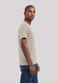 Beige short-sleeve t-shirt, soft fabric, classic crew neck, worn with blue jeans, showing a fitted cut and minimalistic design.
