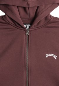 Felpa con cappuccio bordeaux, dotata di zip frontale e logo bianco sul petto. Realizzata in un tessuto morbido e testurizzato per garantire comfort.