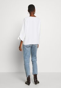 Haut blanc à encolure carrée avec manches évasées, associé à un jean bleu clair aux bords effilochés et des bottines marron foncé.