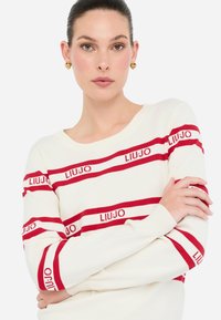 Maglione bianco con strisce orizzontali rosse che presenta il marchio "LIUJO". Collo rotondo, maniche lunghe, polsini a costine. Texture in maglia liscia.
