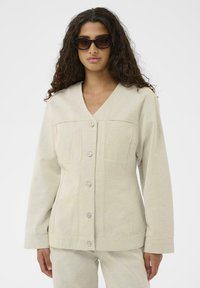 Beige knap-up jakke med V-hals og lange ærmer, lavet af struktureret stof. Har forlommer og en skræddersyet pasform.