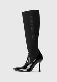 Black knee-high boot featuring a ribbed fabric upper, glossy patent leather toe and heel, pointed shape, and "KARL LAGERFELD" logo detail.