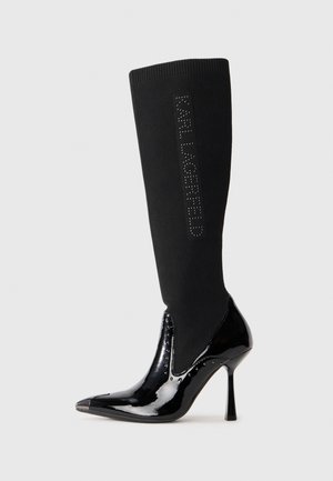 Black knee-high boot featuring a ribbed fabric upper, glossy patent leather toe and heel, pointed shape, and "KARL LAGERFELD" logo detail.