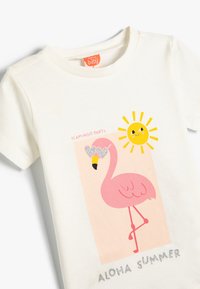 Hvid kortærmet T-shirt med et pink flamingo med hjerteformede solbriller, en gul sol, og teksten "Flamingo Party" og "Aloha Summer."