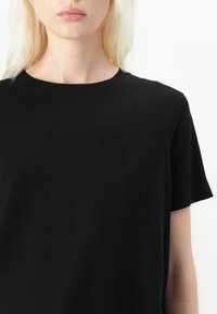 T-shirt noir à manches courtes en tissu tricot doux, avec un col rond et une texture lisse sans motifs ni accents visibles.