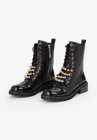 Stivali alla caviglia in pelle nera con dettagli in metallo dorato, lacci, perline decorative e suola in gomma spessa. Cerniera laterale.