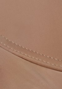 Lichtbruin stof met een gladde textuur, voorzien van een gestikte naad langs de rand, die de gebogen vorm en de zachte afwerking benadrukt.