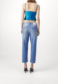 Saténový tyrkysový crop top s tenkými ramínky a detailem knoflíků, spárovaný se světle modrými džíny s uvolněným střihem a kapsami.