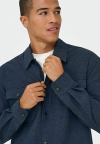 Chaqueta azul marino de botones fabricada con tejido texturizado, que cuenta con dos bolsillos en el pecho, botones a presión negros y cuello con solapa.