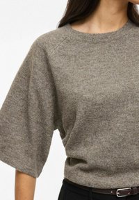 Brūns adīts džemperis ar īsām piedurknēm un apaļu kakla izgriezumu, ar mīkstu tekstūru un brīvu pieguļumu. Kopā ar melnu jostu.