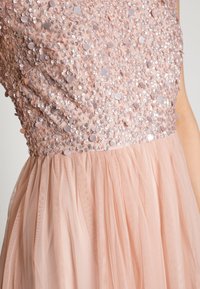 Vestido de noche en rosa empolvado con un corsé de lentejuelas y embellecimientos circulares, y una falda de tul en capas para añadir textura.