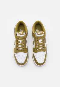 Sneakers Nike con punta e pannelli laterali in pelle bianca, dettagli verde oliva, punta perforata e lacci abbinati. Suola in gomma piatta.