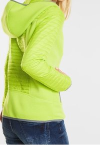 Limetkově zelená bundě na zip s prošívanou texturou na rukávech a horní části zad, s kapucí a šedým lemováním. Měkký, lehký materiál.