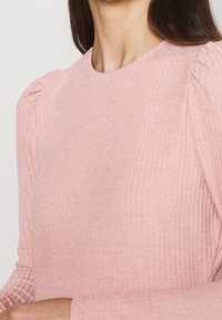 Top a maniche lunghe color rosa chiaro a costine con spalle leggermente imbottite e scollo rotondo con una finitura testurizzata.