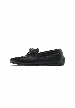 Mocassin en cuir noir avec surpiqûres marron et détail décoratif en lacets, semelle plate et bout arrondi.