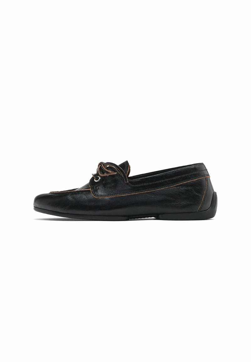 Mocassin en cuir noir avec surpiqûres marron et détail décoratif en lacets, semelle plate et bout arrondi.