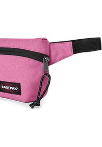 Riñonera de tela rosa con superficie texturizada, cremallera negra y correa ajustable. Cuenta con un parche de logo en la parte frontal.