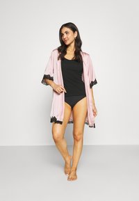 Light pink satin kimono with black lace trim, featuring wide sleeves. Worn over a black tank top and matching black panties.