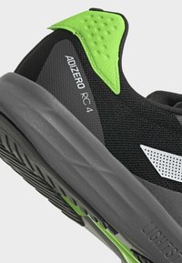 Scarpa da corsa nera con intersuola grigia e accentuazioni verdi. Presenta materiale in rete, tomaia testurizzata e dettagli del logo distintivi.
