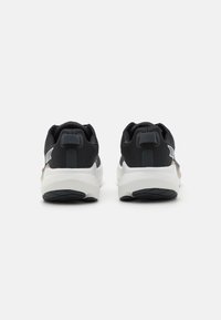 Baskets de sport noires avec une tige texturée, semelle blanche rembourrée et accents réfléchissants, dotées d'un design minimaliste et d'une languette à l'arrière.