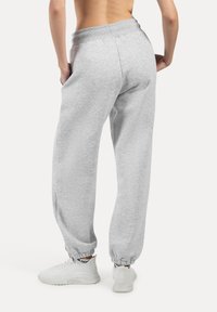 Lichtgrijze sweatpants met een brede elastische tailleband, twee zijzakken en elastische boorden bij de enkels, gecombineerd met witte sneakers.