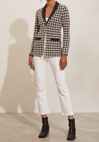 Black and white houndstooth blazer with a black shawl collar, front buttons, and two pockets, paired with white cropped pants and black ankle boots.