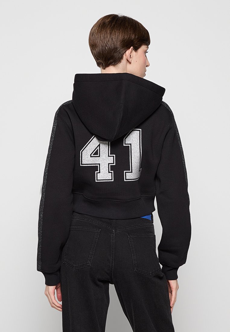 Schwarze, verkürzte Kapuzenjacke mit einer silbernen Zahl "41" auf dem Rücken, runder Kapuze und strukturiertem Akzent an den Ärmeln. Hergestellt aus weichem Stoff, geeignet für die Freizeit.